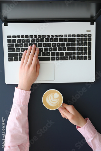 Feminine freelance workspace concept. Woman's hands typing on white laptopp with black keyboard, desk with matte blue table top. Freelance blogger writing an article. Close up, copy space for text. photo