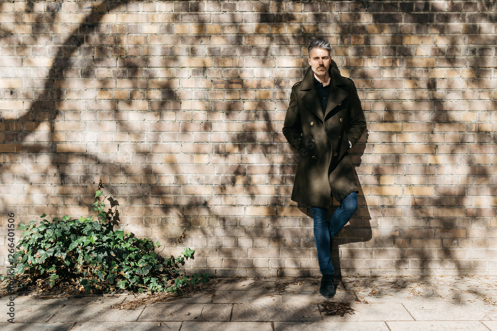 Handsome man in khaki trench coat and jeans over brick wall. Handsome man in khaki trench coat and jeans over brick wall.