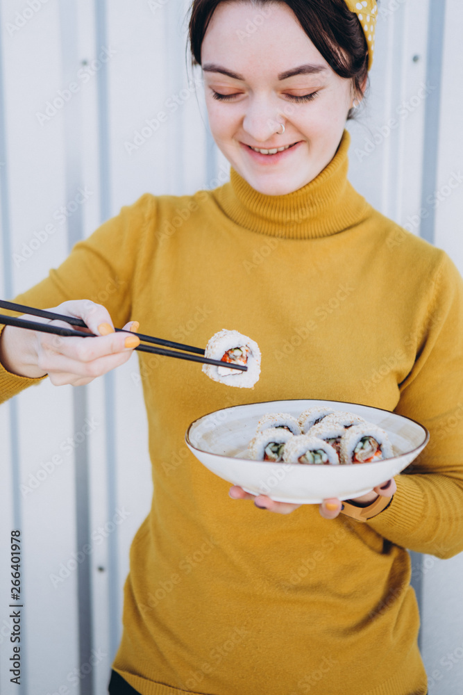 A young beautiful blond girl eating sushi on the summer street urban terrace of a Japanese restaurant A young beautiful blond girl eating sushi on the summer street urban terrace of a Japanese restaurant