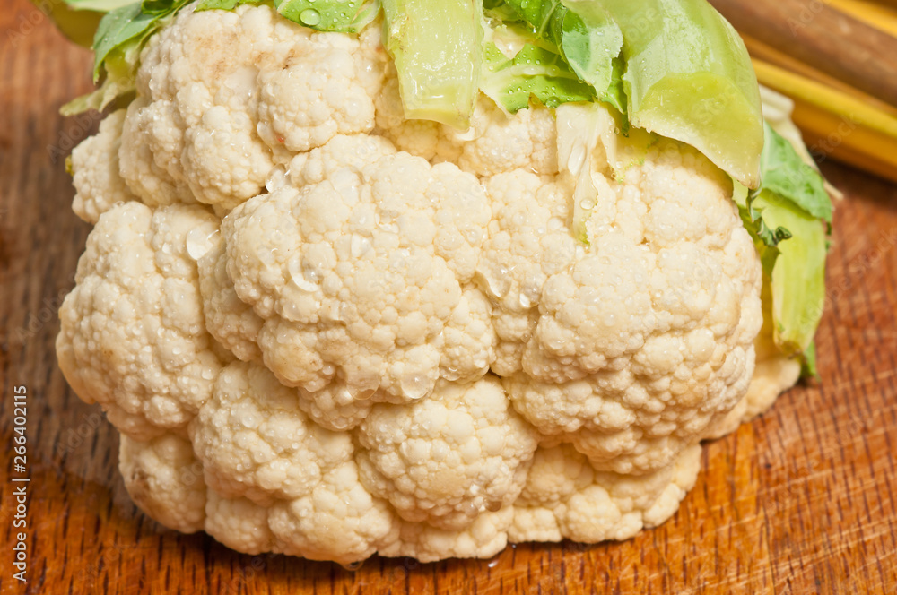 Top view, close up of an organic, local, raw, head of cauliflower with leaves on a wood serving board Top view, close up of an organic, local, raw, head of cauliflower with leaves on a wood serving board