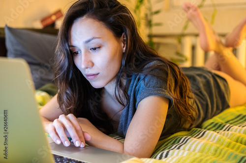 Young woman browsing on her laptop at a bed in a  bedroom photo