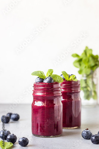Delicious blueberry smoothie with fresh berries and mint in glass jars. Summer healthy drink. Grey stone background. Copy space.