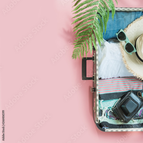 Open suitcase with female clothes for trip on pastel pink. Top view with copy space. Summer concept travel.