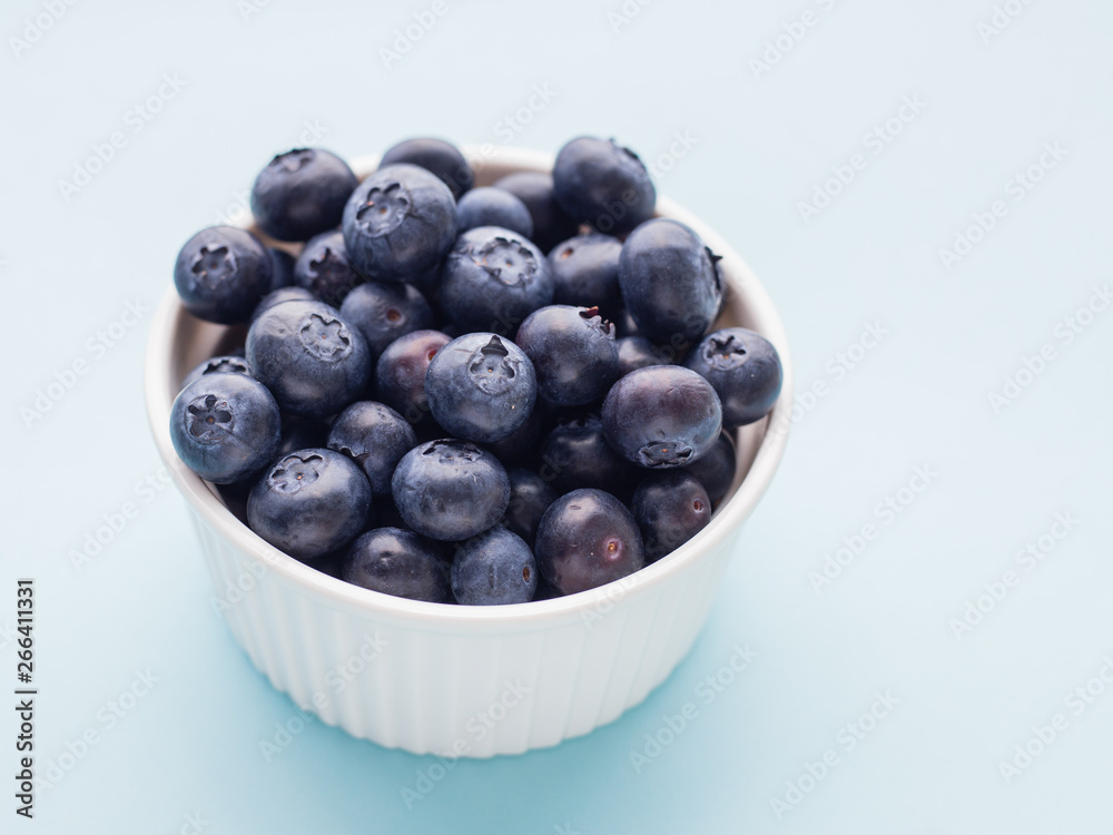 Fresh ripe blueberries in white bowl on a blue bright background Fresh ripe blueberries in white bowl on a blue bright background