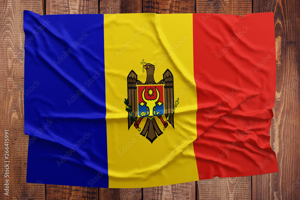 Fototapeta premium Flag of Moldova on a wooden table background. Wrinkled Moldovan flag top view.