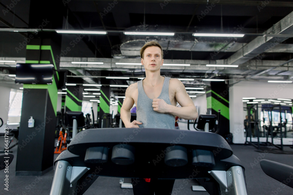 Young man in sportswear running on treadmill at gym Young man in sportswear running on treadmill at gym