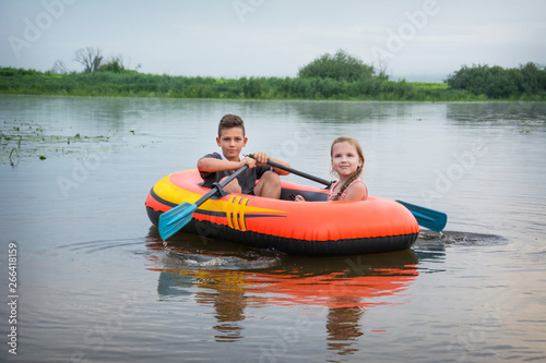 In the summer on the river happy boy with a girl swim in a rubber inflatable boat. © tsomka