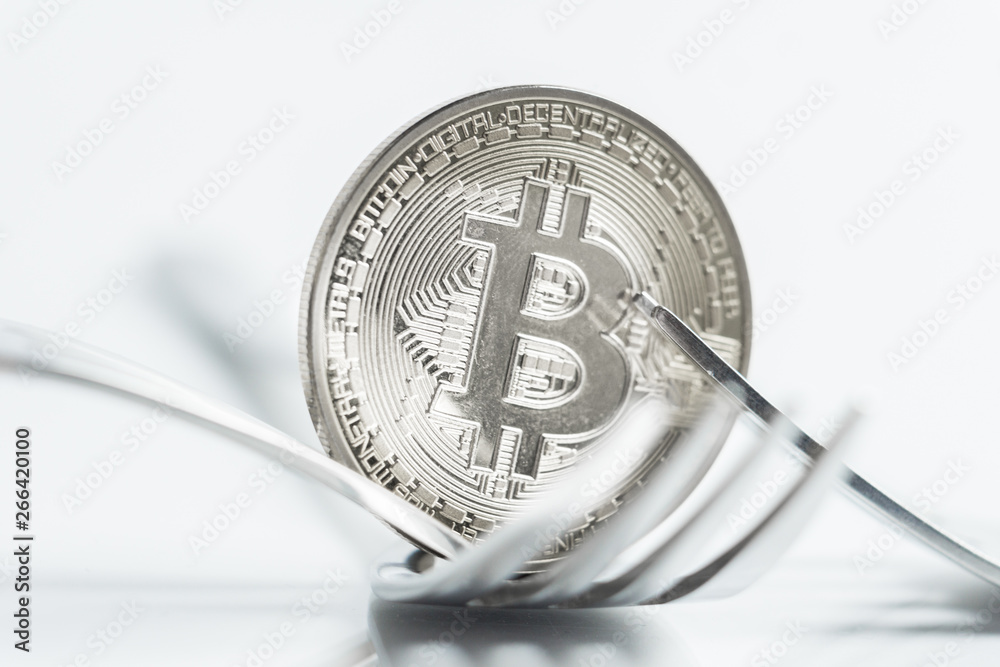 Bitcoin cryptocurreny coin placed between forks with reflection, hard fork Bitcoin cryptocurreny coin placed between forks with reflection, hard fork