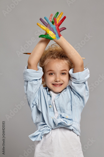 Beautiful little girl with a painted hands is posing on a gray background.