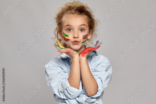 Beautiful little girl with a painted hands and cheeks is posing on a gray background.