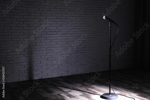 Canvas Print Microphone on dark stage near brick wall. Space for text