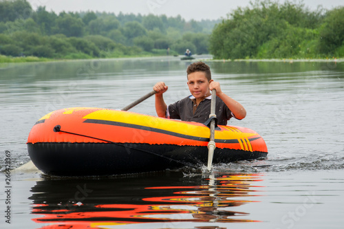 In summer, the boy floats on the river in an inflatable boat. He shows his hand super.