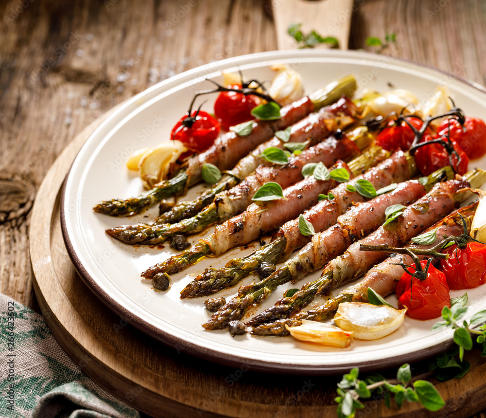 Grilled green asparagus wrapped in ham with the addition of aromatic herbs and spices on a white plate