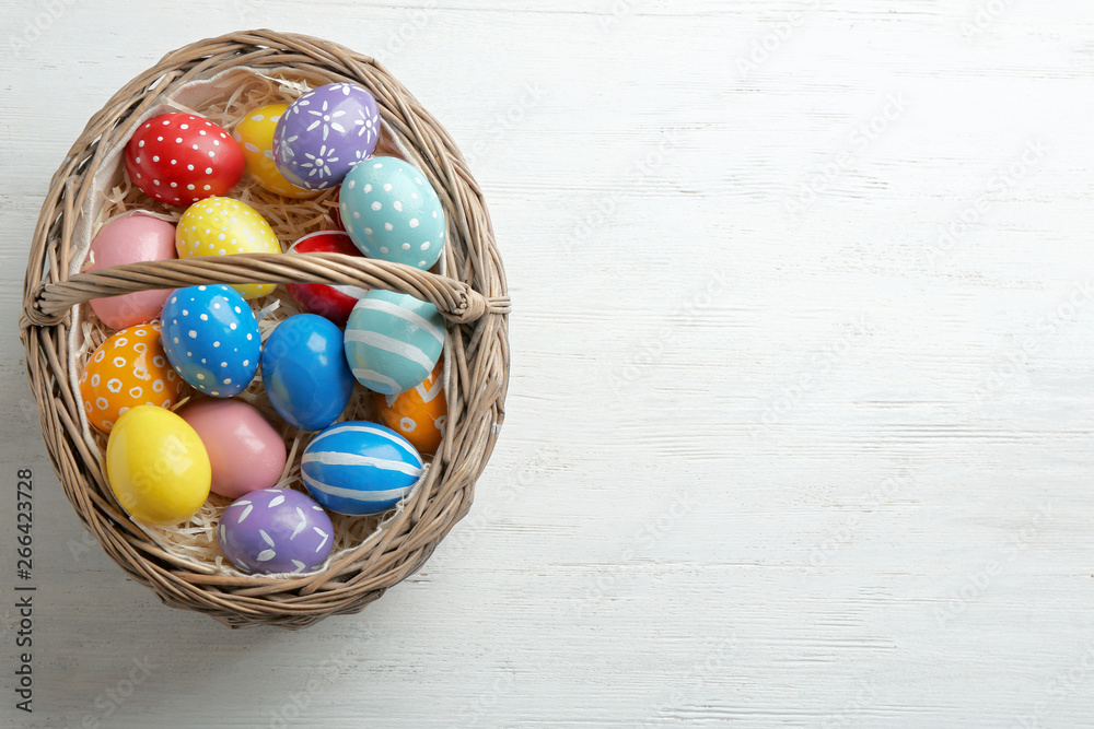 Wicker basket with painted Easter eggs on wooden table, top view. Space for text Wicker basket with painted Easter eggs on wooden table, top view. Space for text