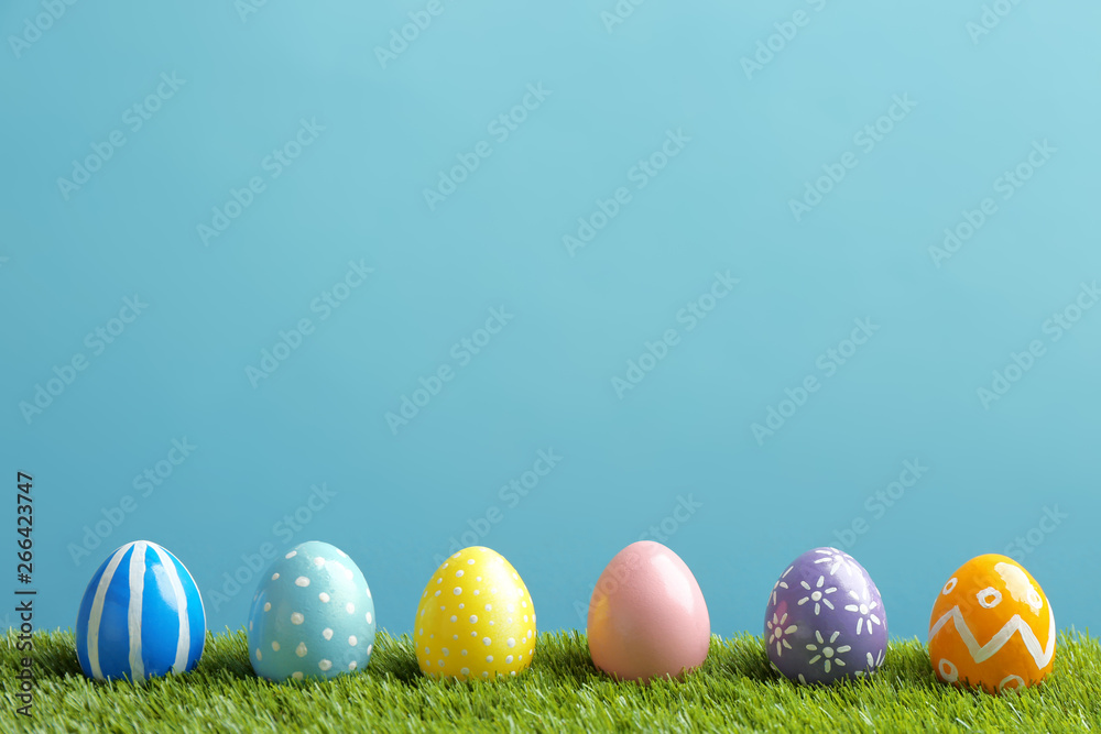 Painted Easter eggs on green grass against color background, space for text