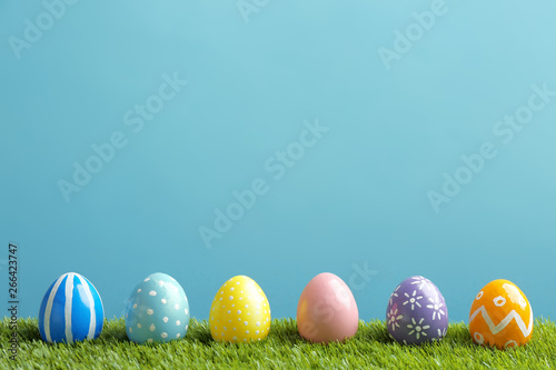 Painted Easter eggs on green grass against color background, space for text