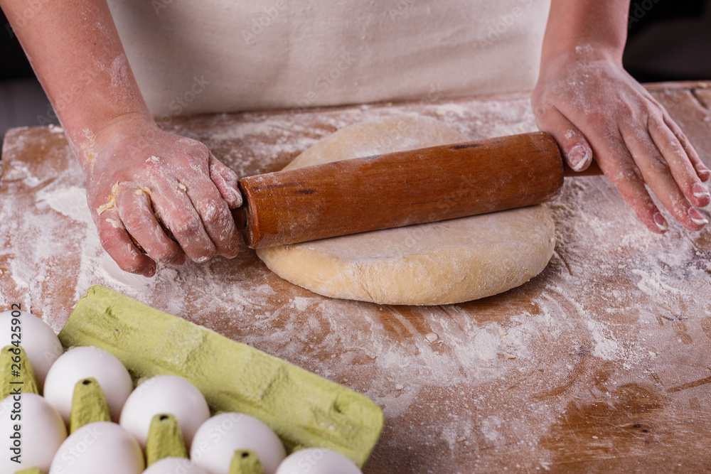 young woman in apron kneading dough on board
