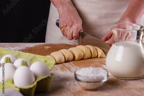 young woman in apron kneading dough on board