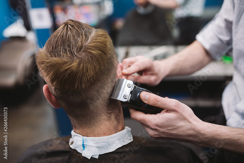 Close up shot of man getting trendy haircut at barber shop. Male hairstylist serving client, making haircut using machine and comb