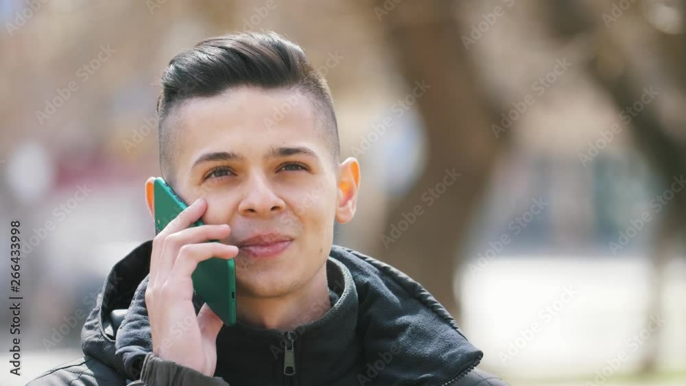Drolling young man chatting on the smartphone and smiling in an alley in spring Drolling young man chatting on the smartphone and smiling in an alley in spring