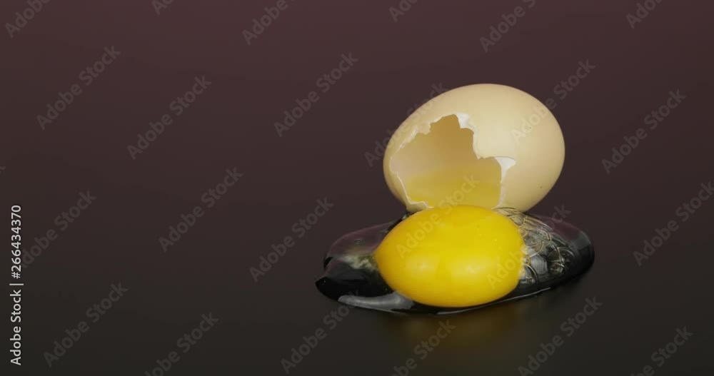Egg yolk poured out from broken eggshell on black surface