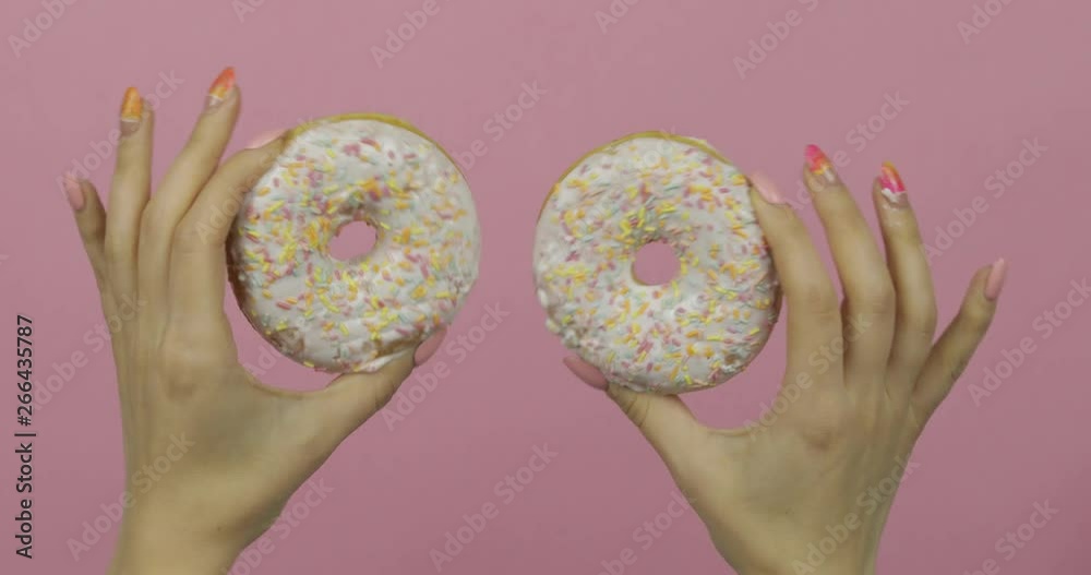 Womens hands holding two white, delicious, sprinkled donuts on pink background. Womens hands holding two white, delicious, sprinkled donuts on pink background.