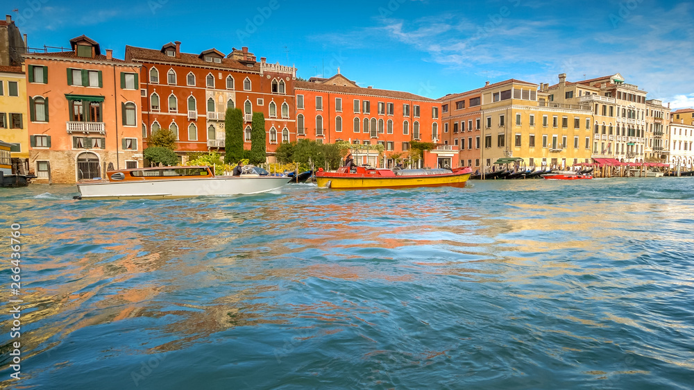 Boats traverse the Grand Canal along amazing city architecture in Venice, Italy, faces blurred for commercial use