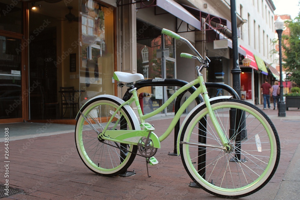 Light green bicycle beside the street on a sidewalk in the shopping district of a charming town.