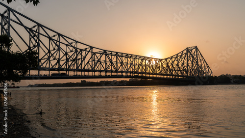 Silhouette of Howrah Bridge at the time of Sunrise.  Howrah Bridge is a bridge with a suspended span over the Hooghly River in West Bengal.