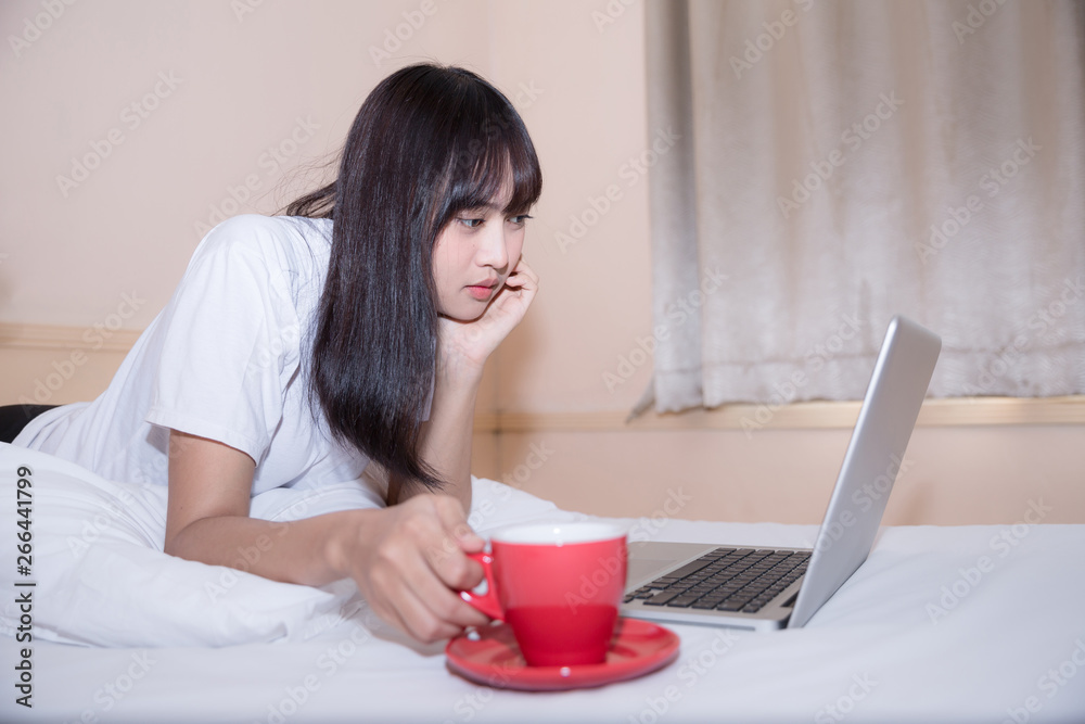 Relaxed young woman sitting on bed with a cup of coffee and laptop Relaxed young woman sitting on bed with a cup of coffee and laptop