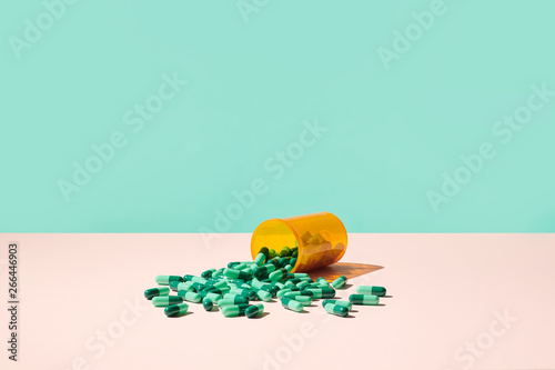 Colorful Prescription Pills Spilling Out of RX Medicine Bottle on Pale Pink Surface  with blue green background. 