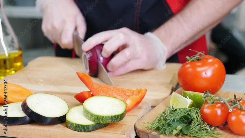 A chef working in the kitchen. Cutting the onion. Different vegetables on the foreground