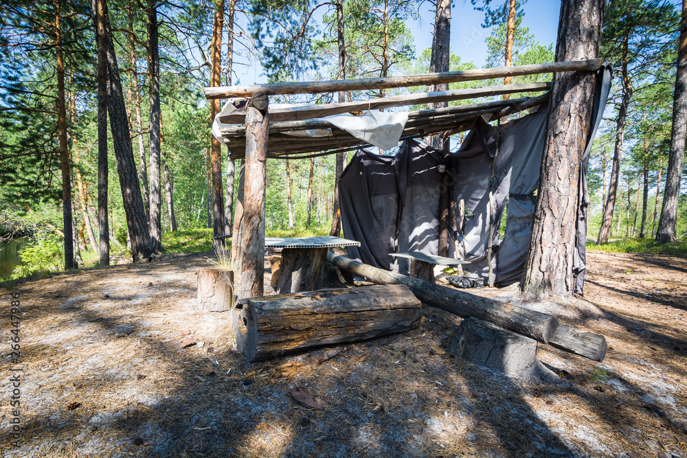 Wooden hut with table and logs in the forest by the river. Wooden hut with table and logs in the forest by the river.