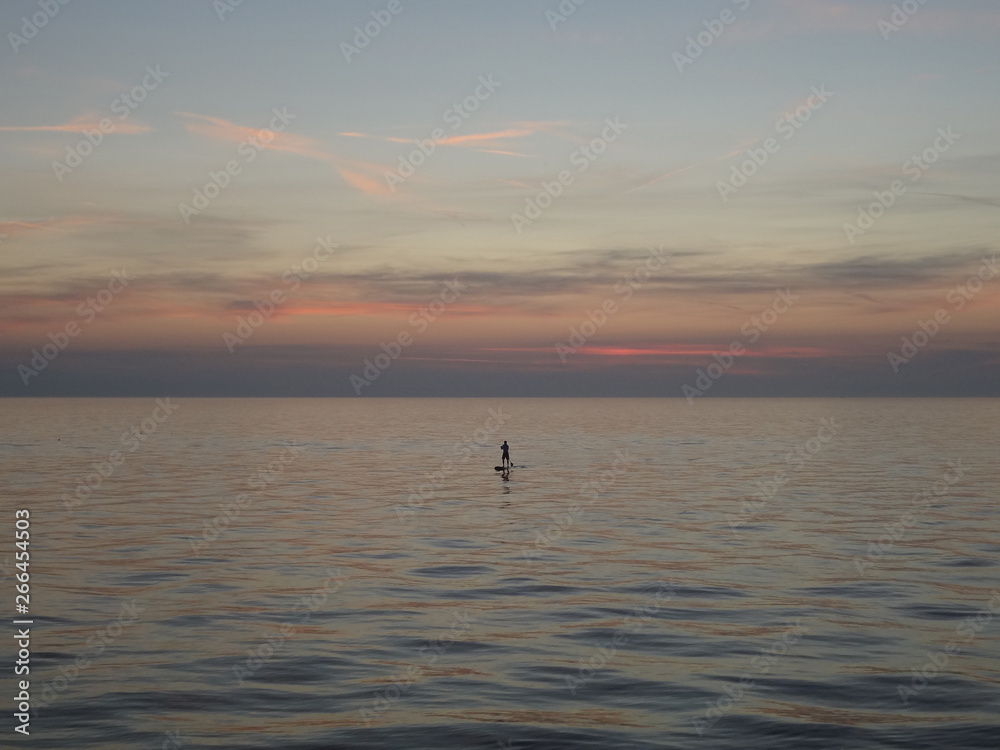 Stand up paddle boarding (SUP) on a big body of water - scenic view on rippling water on lake at sunset