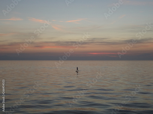 Stand up paddle boarding (SUP) on a big body of water - scenic view on rippling water on lake at sunset