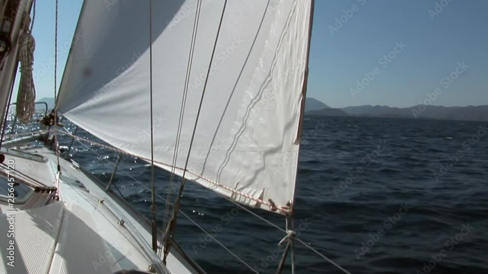 White sails and rope on sailing boat details on deck of moving sailing yacht on background of water surface and blue sky during sea journey. Yachting as an relaxation active lifestyle. White sails and rope on sailing boat details on deck of moving sailing yacht on background of water surface and blue sky during sea journey. Yachting as an relaxation active lifestyle.