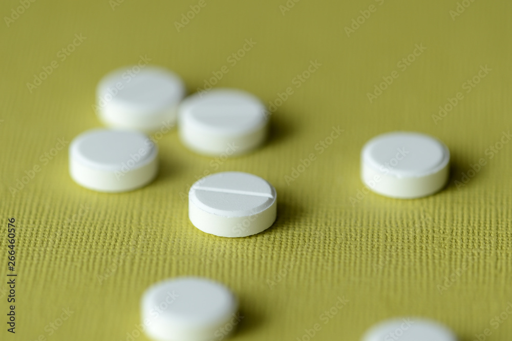 White tablets scattered on a green-yellow background close up White tablets scattered on a green-yellow background close up