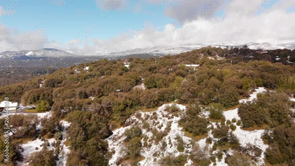 Aerial shot ascending up a hill covered in fresh winter snow revealing mountains and partly cloudy sky in the background Aerial shot ascending up a hill covered in fresh winter snow revealing mountains and partly cloudy sky in the background