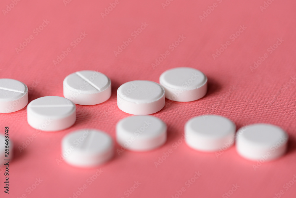 White tablets scattered on a pink background close up White tablets scattered on a pink background close up