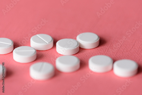 White tablets scattered on a pink background close up