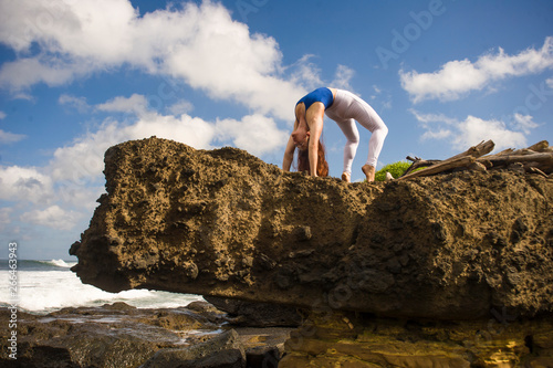young attractive and concentrated woman practicing acroyoga balance exercise and yoga flexibility and meditation at beautiful beach rock cliff in healthy lifestyle