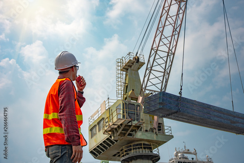 worker stevedore foreman, engineering, loading master talks to crane driver by walkie talkie for safety lifting the goods shipment, lifting by gantry crane, working at risk on the high level insurance