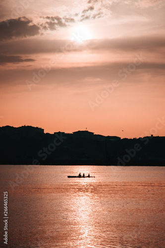 three people in a canoe with the sunset in the middle of the sea