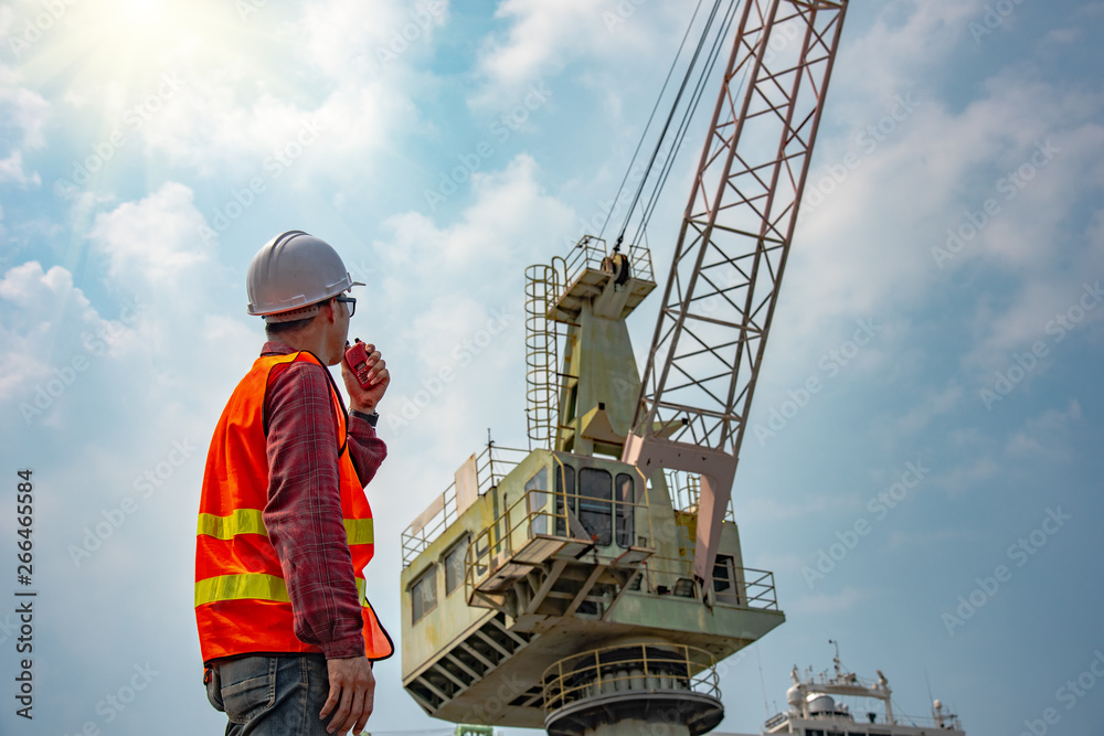 worker stevedore foreman, engineering, loading master talks to crane driver by walkie talkie for safety lifting the goods shipment, lifting by gantry crane, working at risk on the high level insurance worker stevedore foreman, engineering, loading master talks to crane driver by walkie talkie for safety lifting the goods shipment, lifting by gantry crane, working at risk on the high level insurance