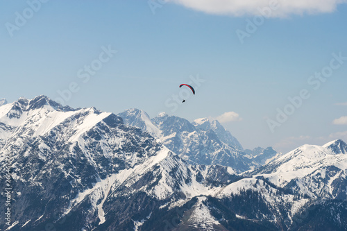 Paragliding over Alps on a sunny day with mountain cliffs covered with snow in Tirol Austria.