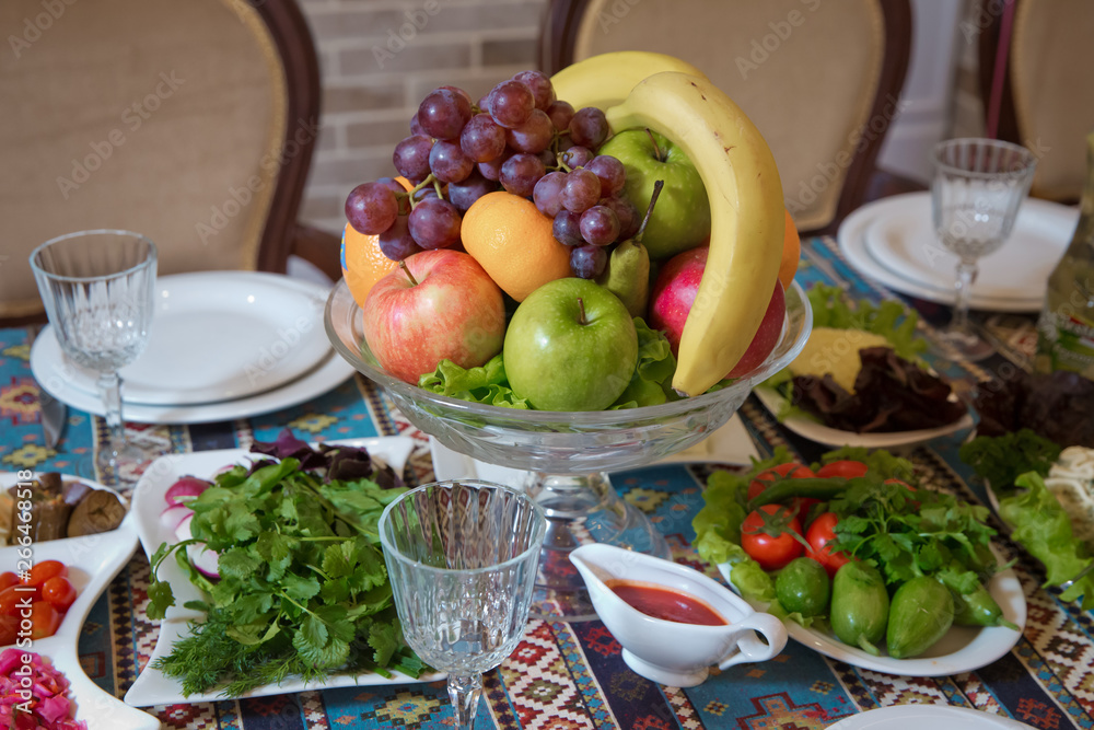 Fruit in a bowl .Red and blue apple, orange, red banana banana. Cucumber, tomato, greens, radish.