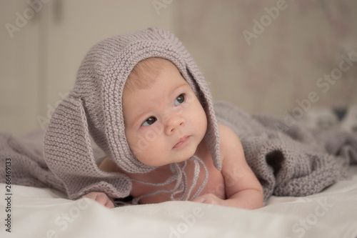 A small child of 1 months in a gray hat with ears looks to the side. Soft light soft focus