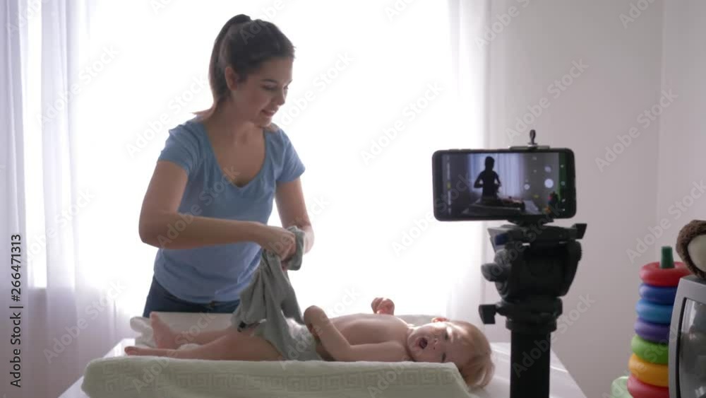 happy motherhood, popular vlogger woman changes clothes of baby boy while recording teaching video on mobile phone for subscribers in social networks in live broadcast at home happy motherhood, popular vlogger woman changes clothes of baby boy while recording teaching video on mobile phone for subscribers in social networks in live broadcast at home