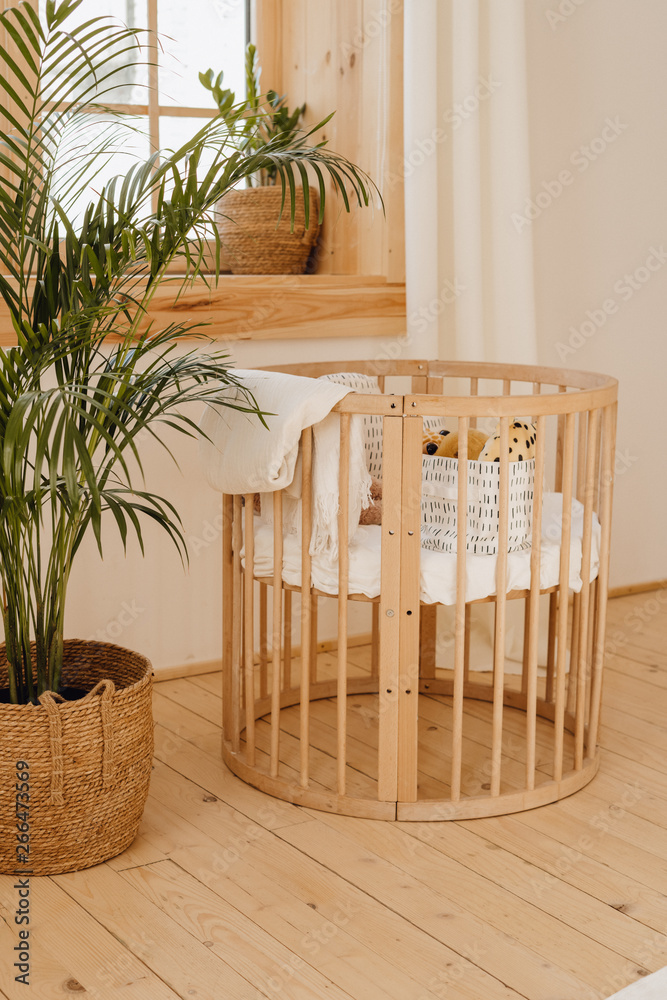 Wooden Baby Bed Crib in Eco Friendly Cozy Interior. Light Brown Childish Bedroom with Wood Empty Cot. Cosy Home Hygge Style Design. Beautiful Infant Toy in Small Round Cot at Cottage Background Wooden Baby Bed Crib in Eco Friendly Cozy Interior. Light Brown Childish Bedroom with Wood Empty Cot. Cosy Home Hygge Style Design. Beautiful Infant Toy in Small Round Cot at Cottage Background
