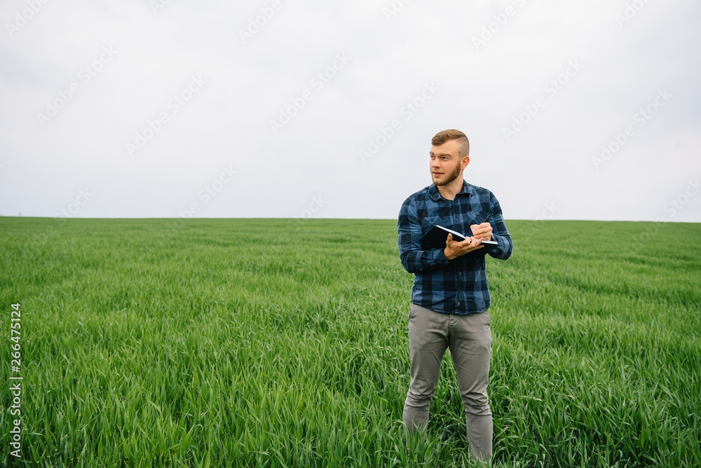 Young agronomist holds notebook in green wheat field. Agribusiness concept. agricultural engineer standing in a wheat field with a tablet in summer